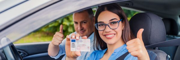 Driving school. Beautiful young woman successfully passed driving school test. She looking sitting in car, looking at camera and holding driving license in hand. Girl with driving license