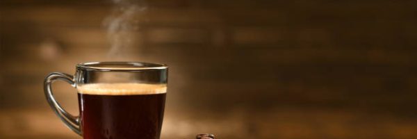 Cup glass of coffee with smoke and coffee beans on old wooden background