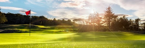 Golf course putting green with flag at sunset or sunrise