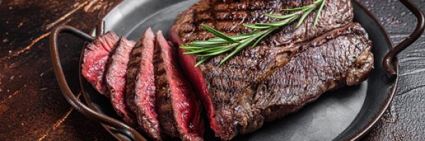 Grilled Medium Rare top sirloin beef steak or rump steak on a steel tray. Dark background. Top view.