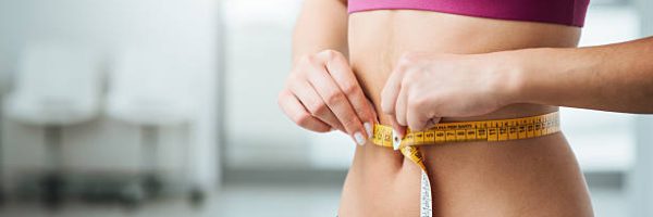 Slim young woman measuring her thin waist with a tape measure, close up