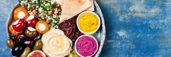 Middle Eastern meze platter with green falafel, pita, sun dried tomatoes, pumpkin and beet hummus, olives, stuffed peppers, tabbouleh, figs. Mediterranean appetizer party idea