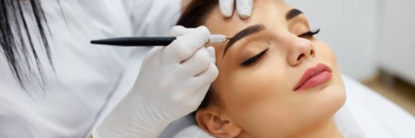 Permanent Makeup For Eyebrows. Closeup Of Beautiful Woman With Thick Brows In Beauty Salon. Beautician Doing Eyebrow Tattooing For Female Face. Beauty Procedure. High Resolution